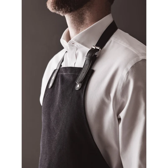 Stylish and classic apron in thick cotton canvas with discreet details in vegan leather. Adjustable buckle closure at the top and large pocket in the front. An apron with a long lifespan that only gets more beautiful with time. (VG019-03)-1